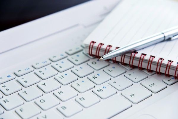 A notepad and pen on top of a computer keyboard